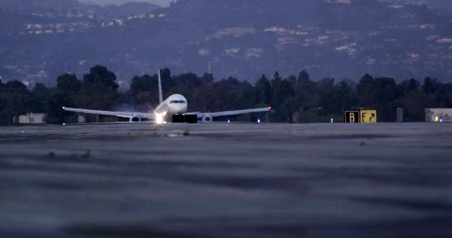 An airplane descends from the air and lands on an airstrip at an airport near mountains