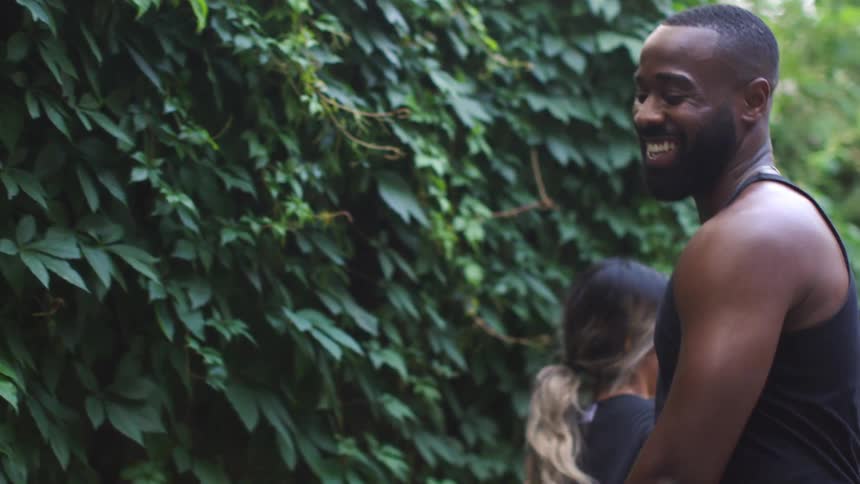 Man and woman greet each other with clasped hands and a hug as they pass by near vine covered wall