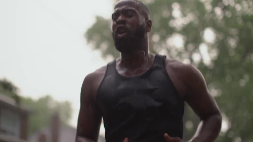 A black man is jogging in a neighborhood during the day with rain falling