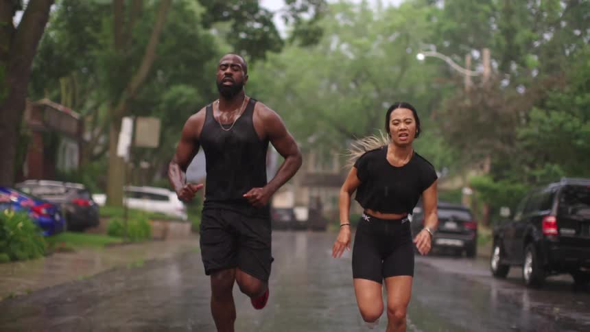 A woman and a man run in the street while it rains