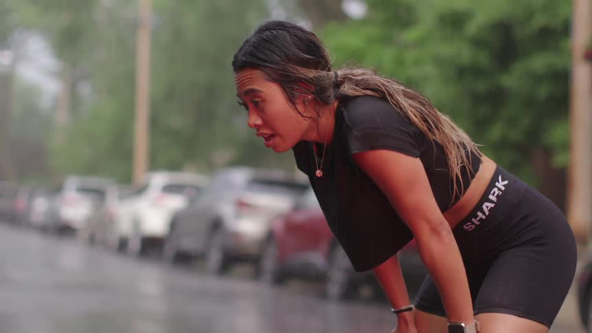 Woman leaning over taking a breath in the middle of a run in the rain
