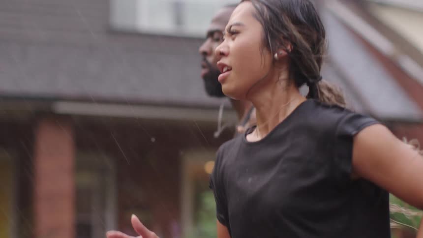 Man and a woman running together outside in a street in the rain