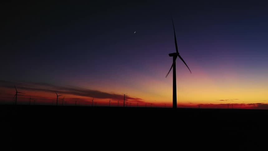 A wind turbine spins slowly on a wind farm at sunset