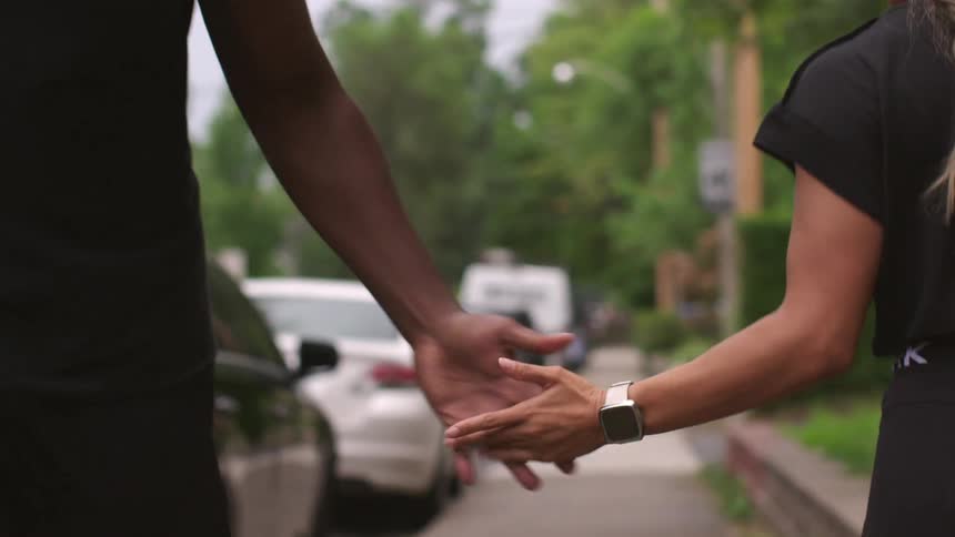 A man and a woman walking and giving each other five in a neighborhood with vehicles trees the sky and clouds in the background
