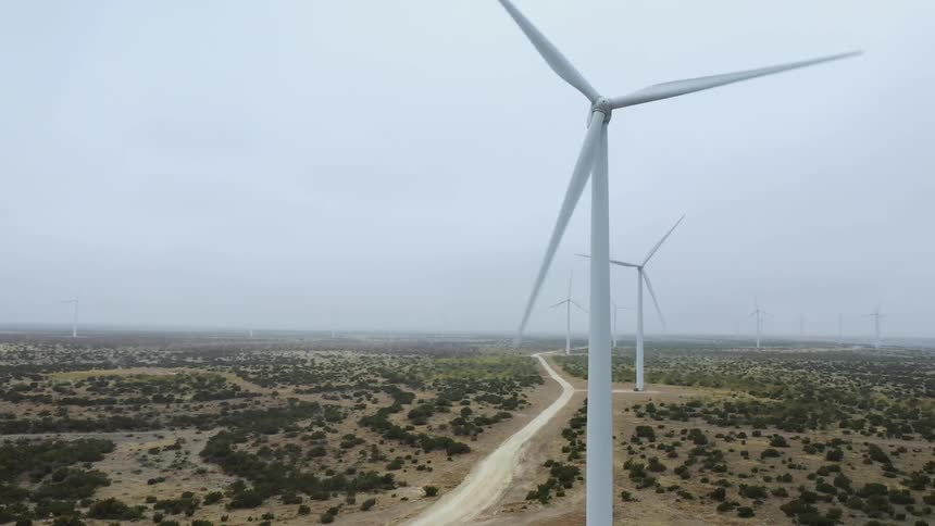 A dirt road lined by wind turbines with a flat landscape