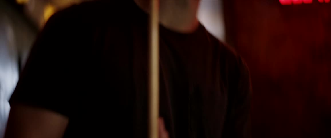 A young man laughs as he holds a pool cue in a bar