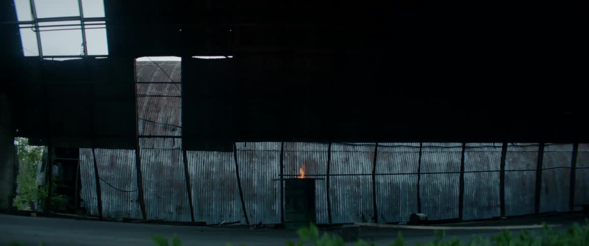 Fire burns in a barrel in a derelict rounded tin barn during the day