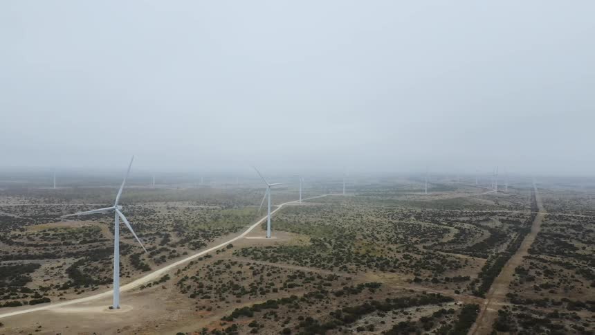 Wind turbines spin next to a road on a foggy day