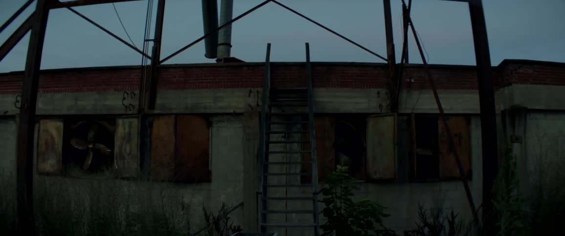 Outside of an abandoned building with a small metal staircase leading to the roof