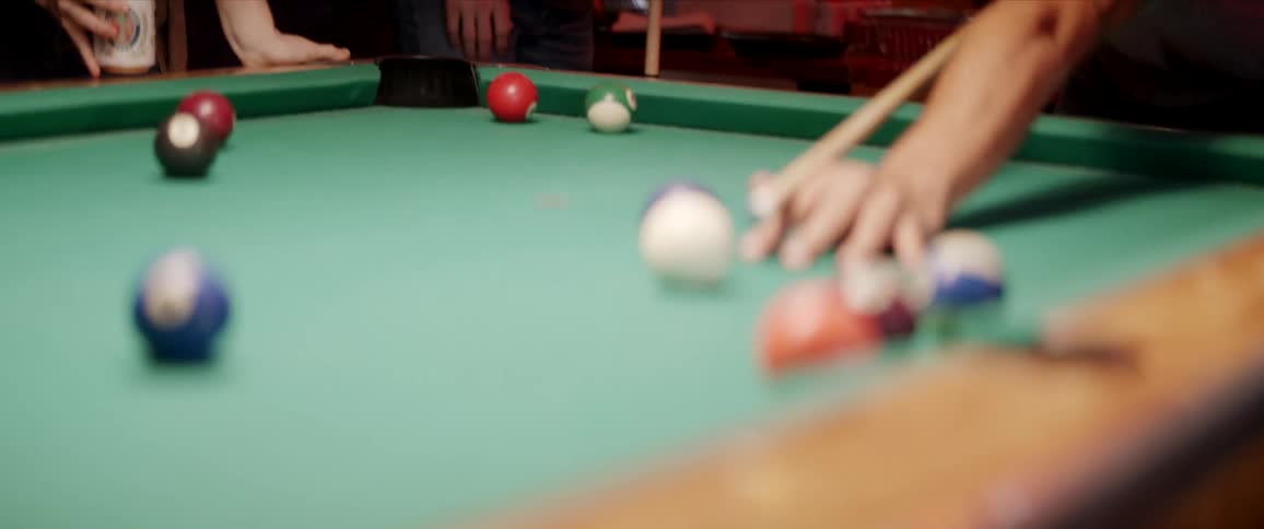 A man strikes a cue ball with a pool cue in a bar