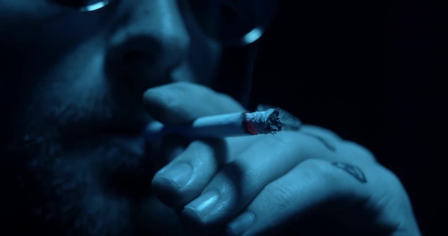 Man smokes under light surrounded by darkness