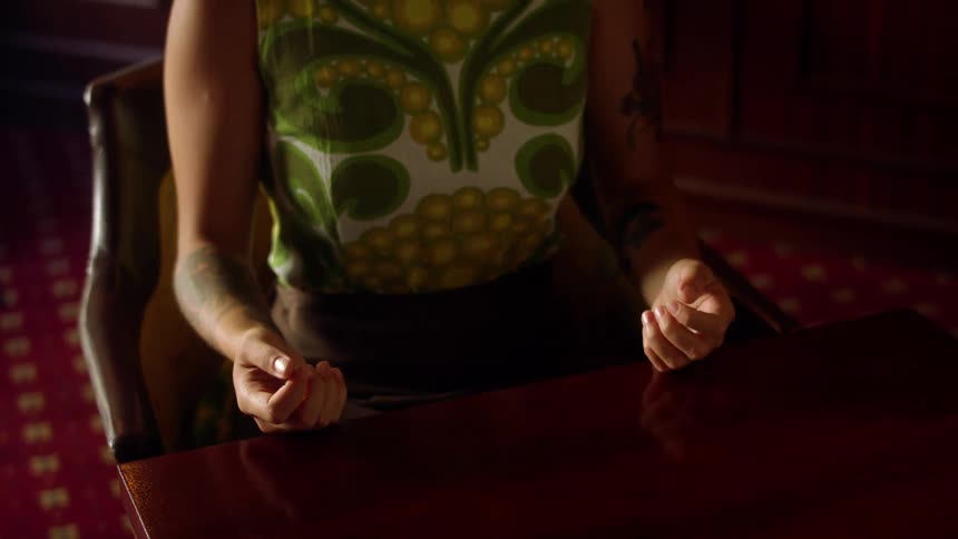 A tattooed woman takes deep breaths while sitting at a table indoors