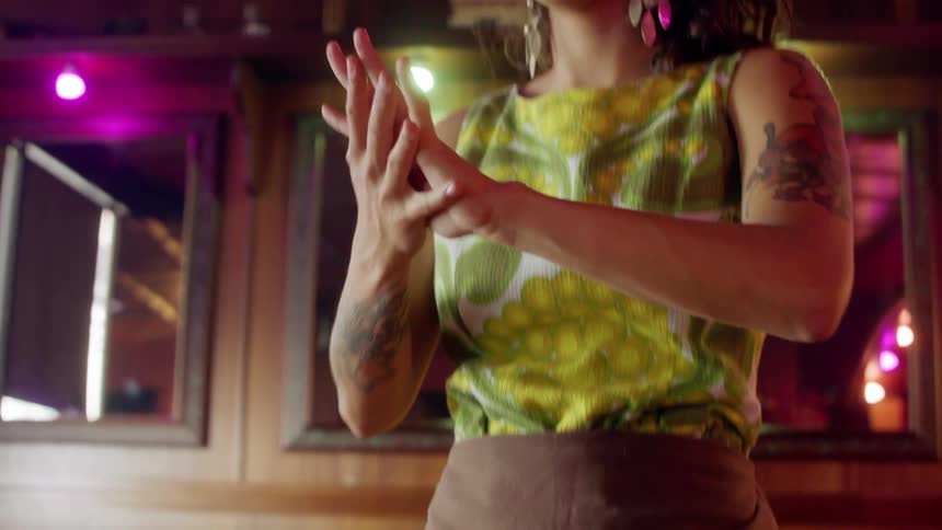 A young woman wearing a green retro dress and apron does an artistic dance with her hands in a restaurant
