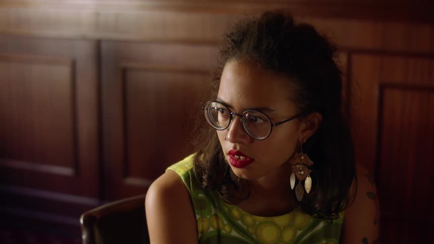 A black woman sits on a chair looking at someone and then putting her head down