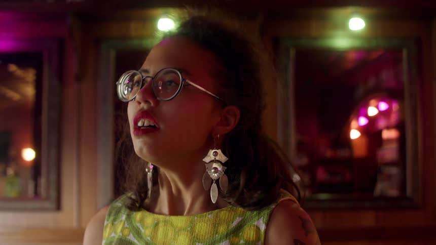 A woman with glasses and earrings breathing in a room with mirrors in the background