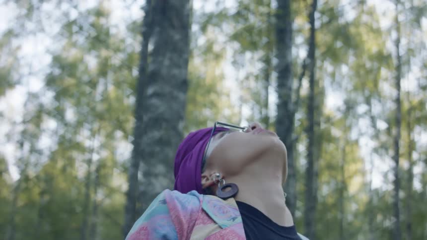 A young woman in colorful clothing dances in a woodland during the day