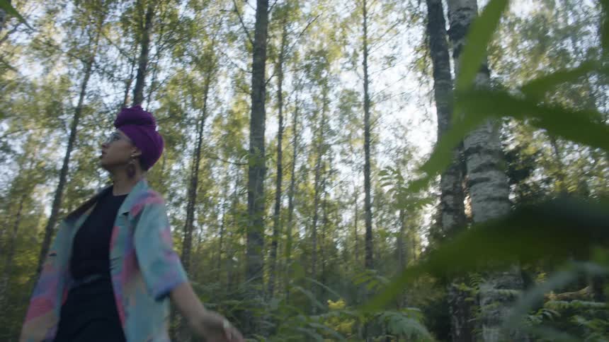 A black woman performs a modern dance routine in the middle of a forest during the day