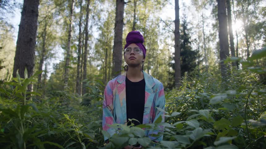 A black woman stands in a forest during the day