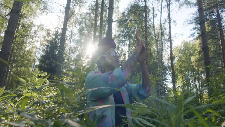 A woman stands in a forest touching her arms with her hands in the daytime