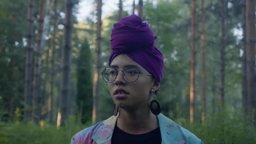 A teenage girl in a forest looks up to the sky and looks around and holds on to her head