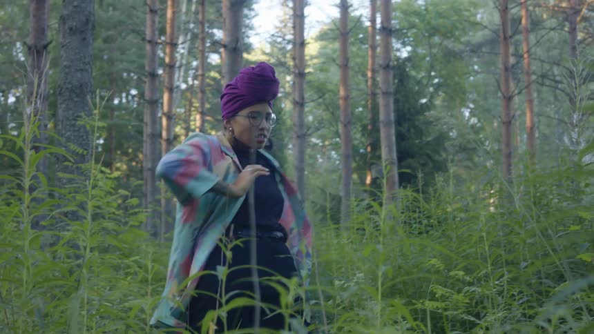 A black woman is performing a modern dance routine in the forest during the day