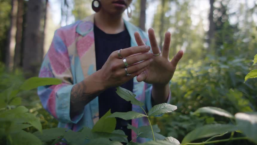 Woman wearing turban stands in forest clearing examining her hands