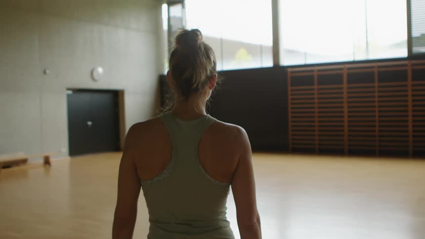 A woman walks into a yoga studio while holding a yoga mat