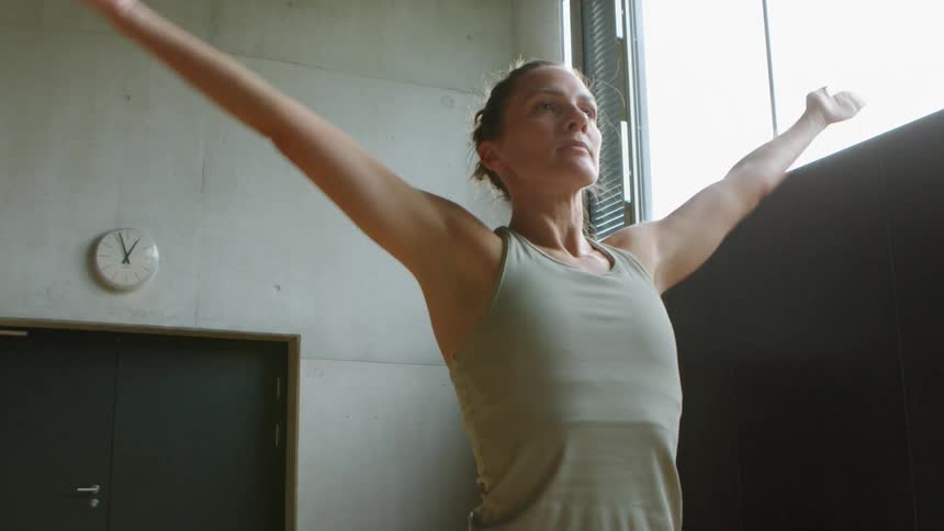 A woman stretches down and raises her arms above head in a gym indoors