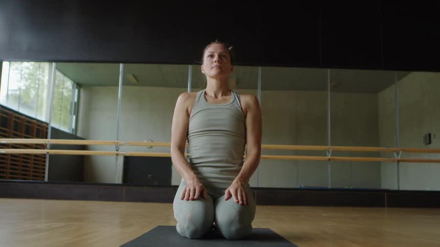 Woman with a grey sport top and leggings does stretches on a yoga mat in the gym