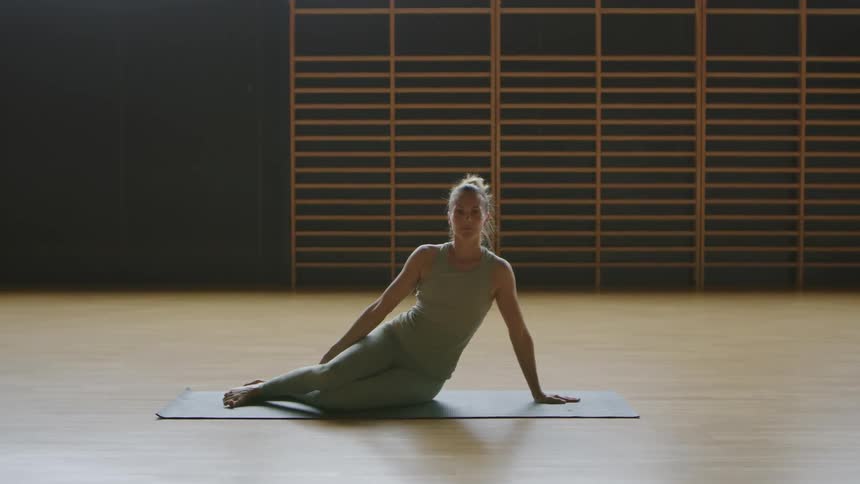 A woman does yoga poses on a yoga mat in a large room