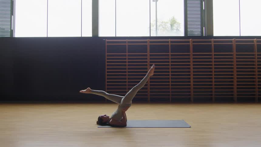 A woman does exercising on a yoga mat in a large room during the day