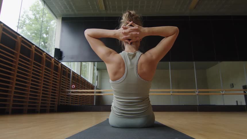 Woman with a grey sport top and leggings works out on a grey yoga mat in the gym