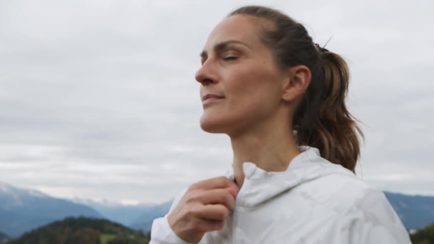 Woman wearing a white jacket preparing to run outside on a hilltop