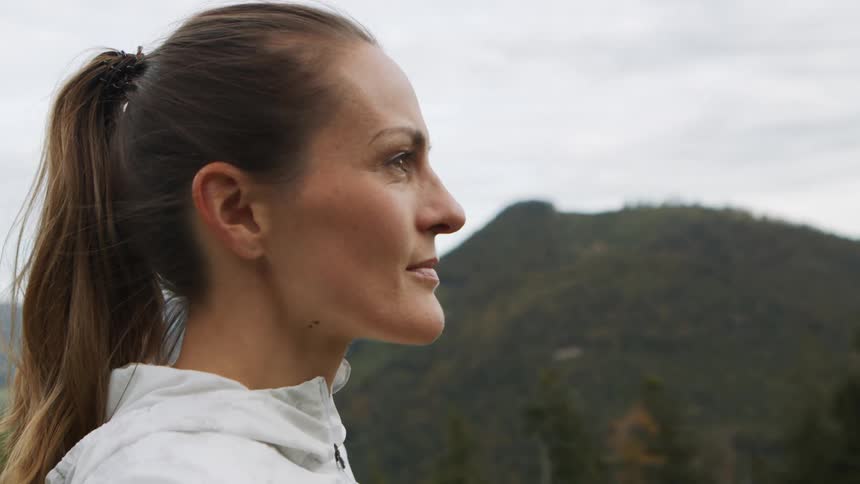 Woman with a ponytail and a white zip up hoodie looks at the mountains after workout