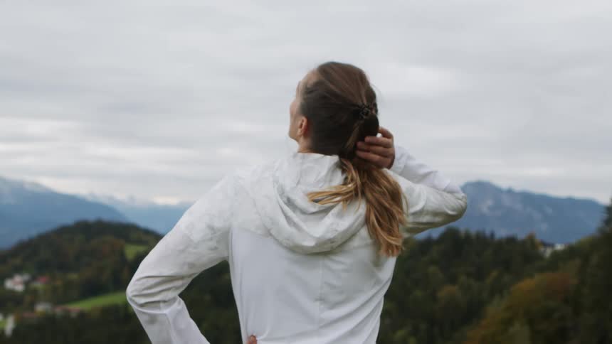Woman stands looking out over forests covered mountains and misty horizon