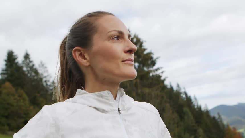 Woman with a ponytail and a white zip up hoodie looks at the mountains after workout