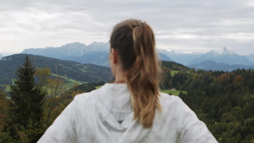 A young woman standing in the mountains looks out over the forested countryside below