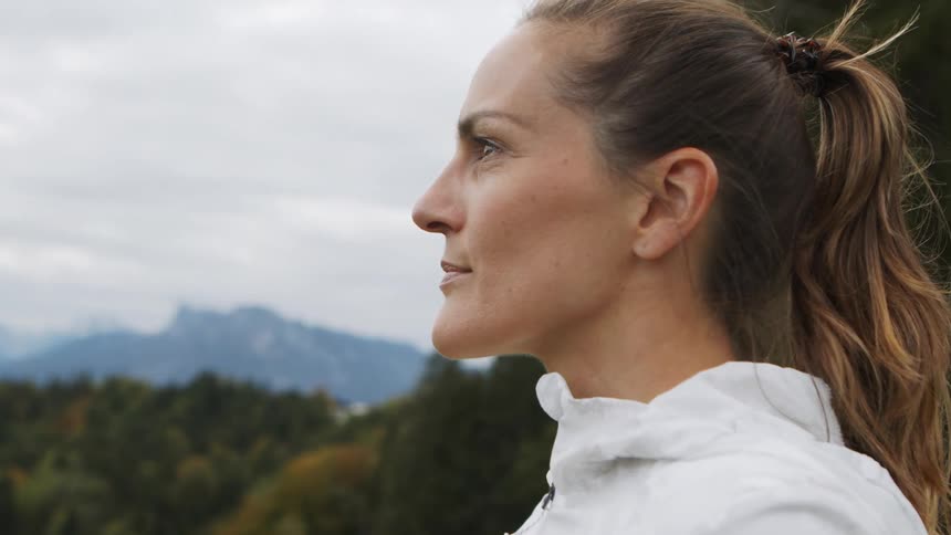 Woman with a ponytail and a white zip up hoodie looks at the mountains after workout