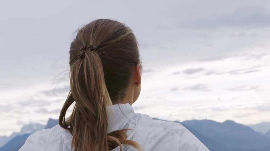 Woman with a ponytail and a white zip up hoodie looks at the mountains after workout