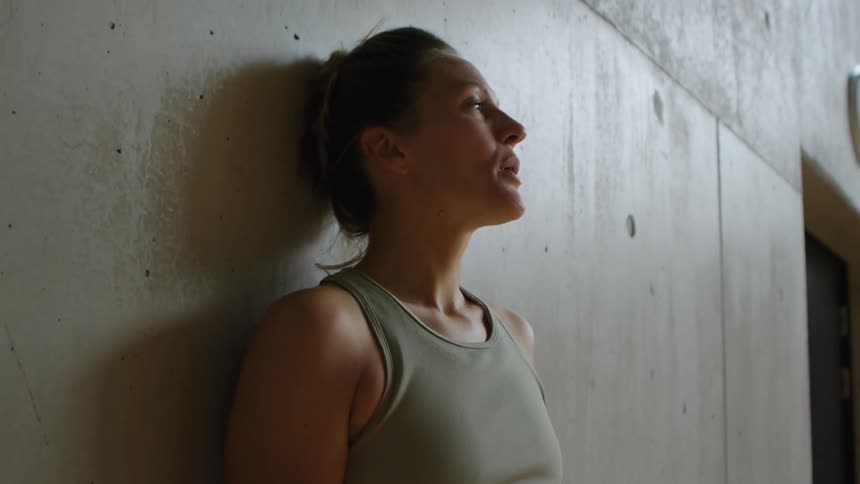 A woman walking up to and leaning on a wall after workout