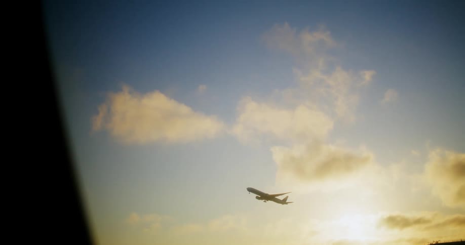 An airplane ascends in the sky with clouds and a low sun