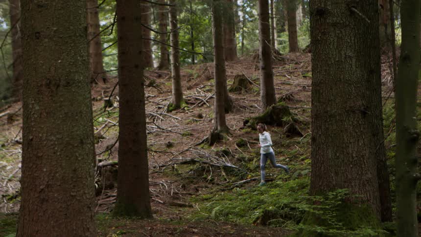 A woman jogs through a forest during the day