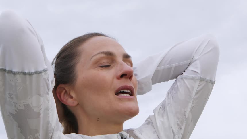 Woman standing with her hands behind her head taking a deep breath