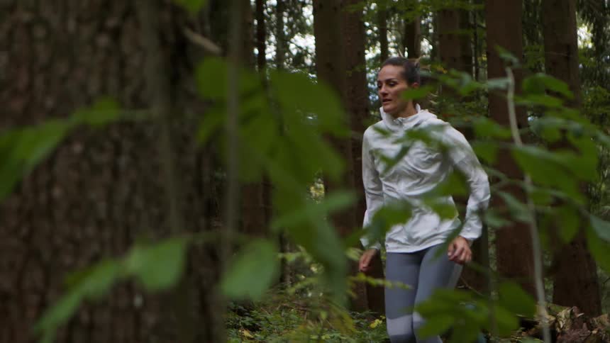 A white woman is running through a forest in overcast conditions