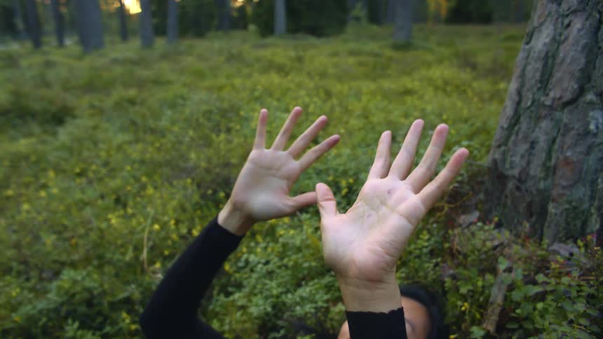 Woman laying down in a grass field in the forest twirling her hands upwards