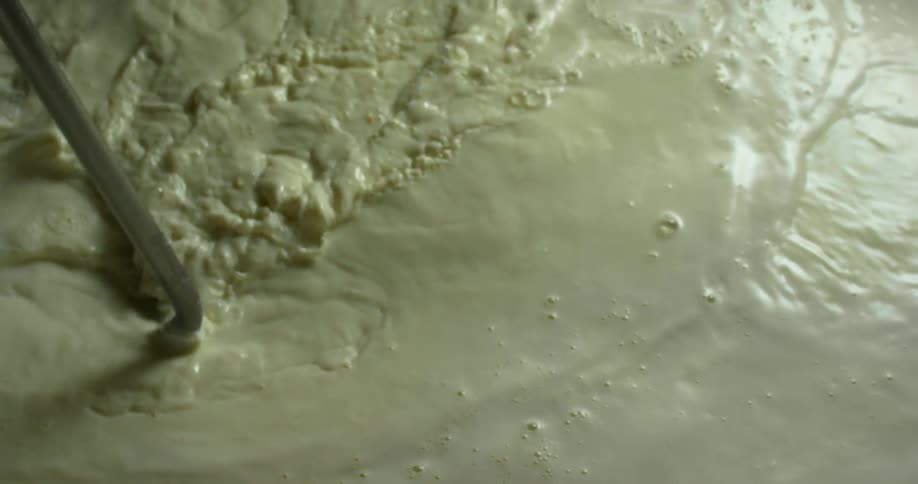 A creamy green liquid with bubbles being stirred with a pole