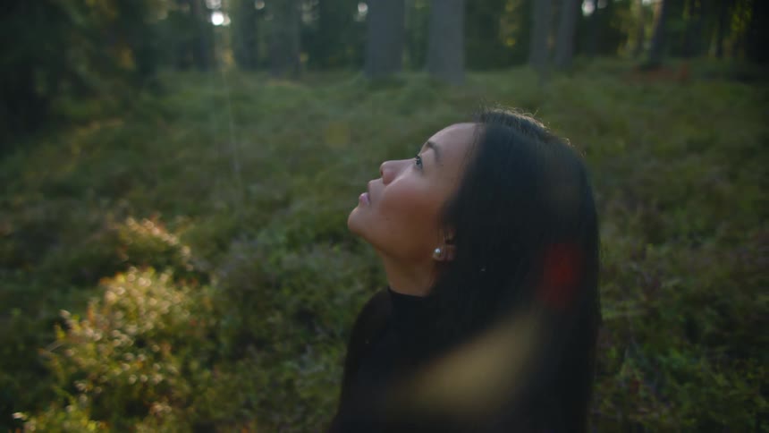 A woman looks to the sky in forested area