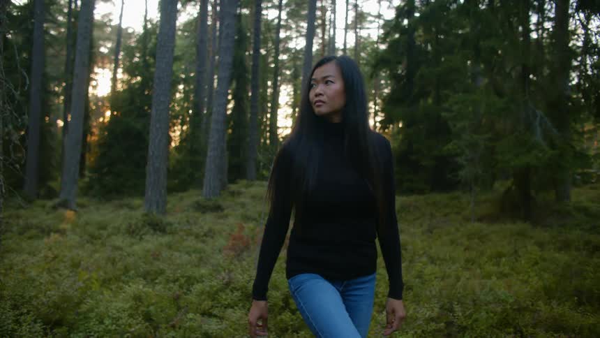 A woman walking in the woods looking at the sky with trees the sky and clouds in the background