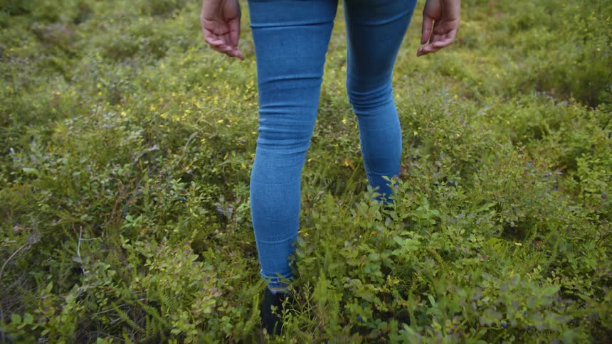 A woman walks through a field in jeans and boots during the day