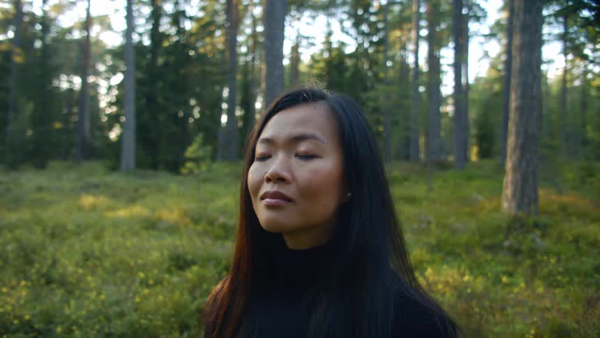 Woman wearing long sleeve blackturtle neck shirt stands in clearing in forest during the day